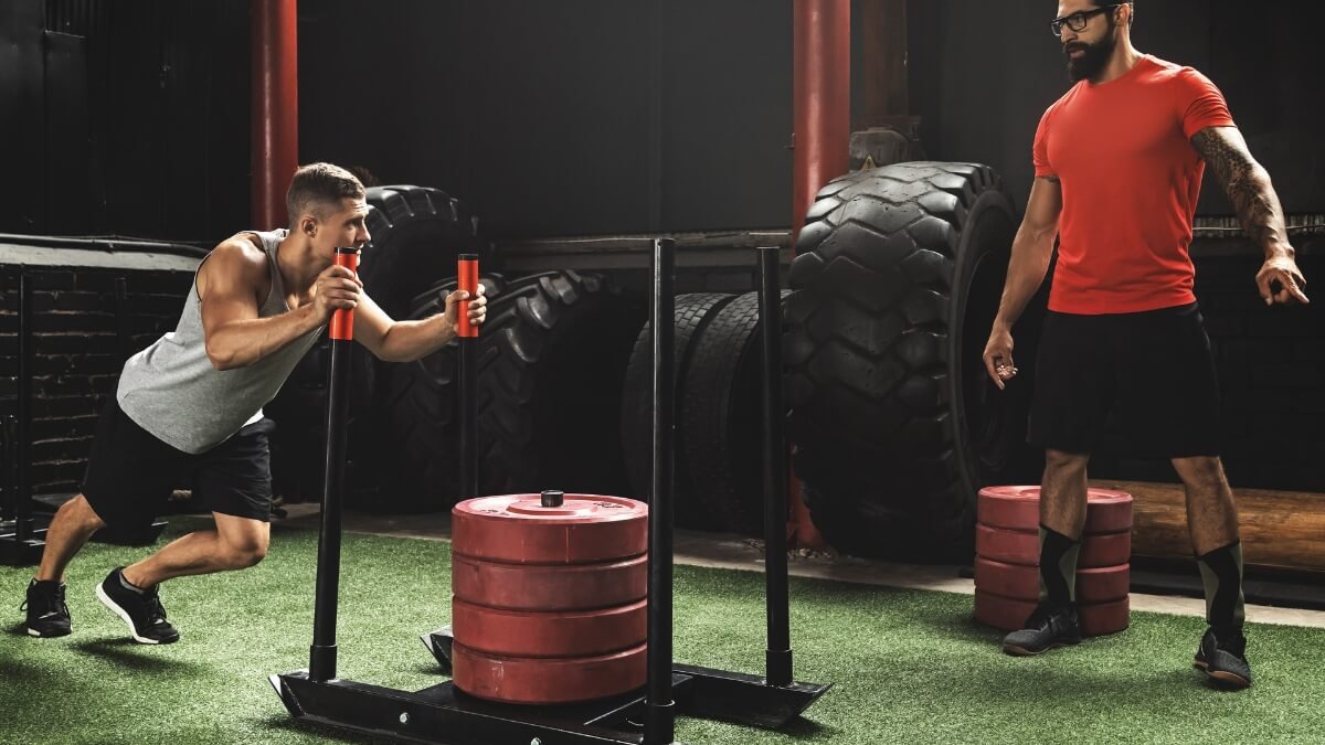 Svertinių Rogių Treniruotės (Sled Training). Sportininkas treniruojasi su treneriu naudojant svertines roges.