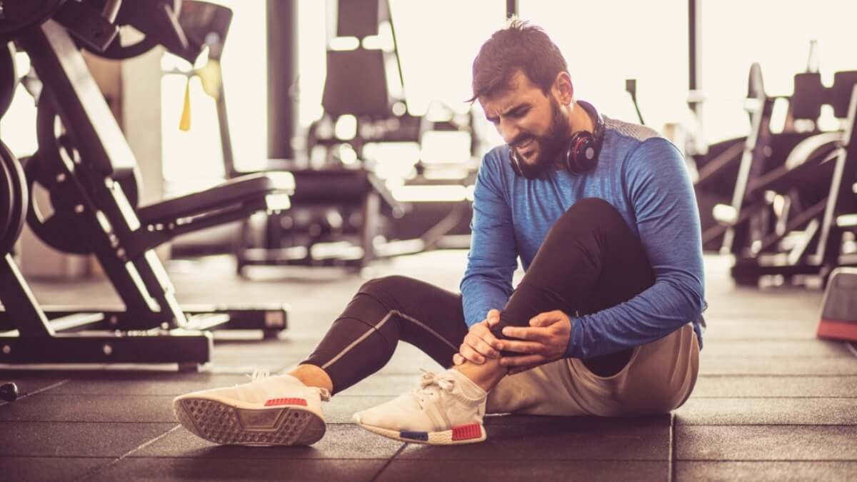 Apžvelgimas apšilimas sužalojimų prevencijai (Warm-Up For Injury Prevention). Paveiksliuke atvaizduotos vyras gulintis ant žemės ir susiėmęs už skaudančios kojos.
