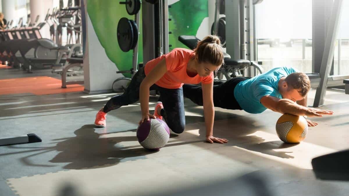 Medicininio Kamuolio Pratimų Veiksmingumas (Medicine Ball). Pateikta iliustracija kur mergina ir vaikinas naudoja medicininį kamuolį atsibaudimams nuo žemės.