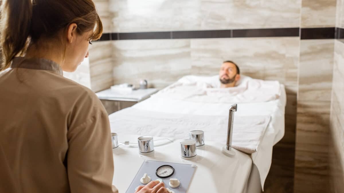 Angliarūgštės Mineralinė Vonia (Carbonated Mineral Bath). Specialistė paruošia vonią, kurioje vyrui yra atliekama angliarūgštes mineralinė procedūra.