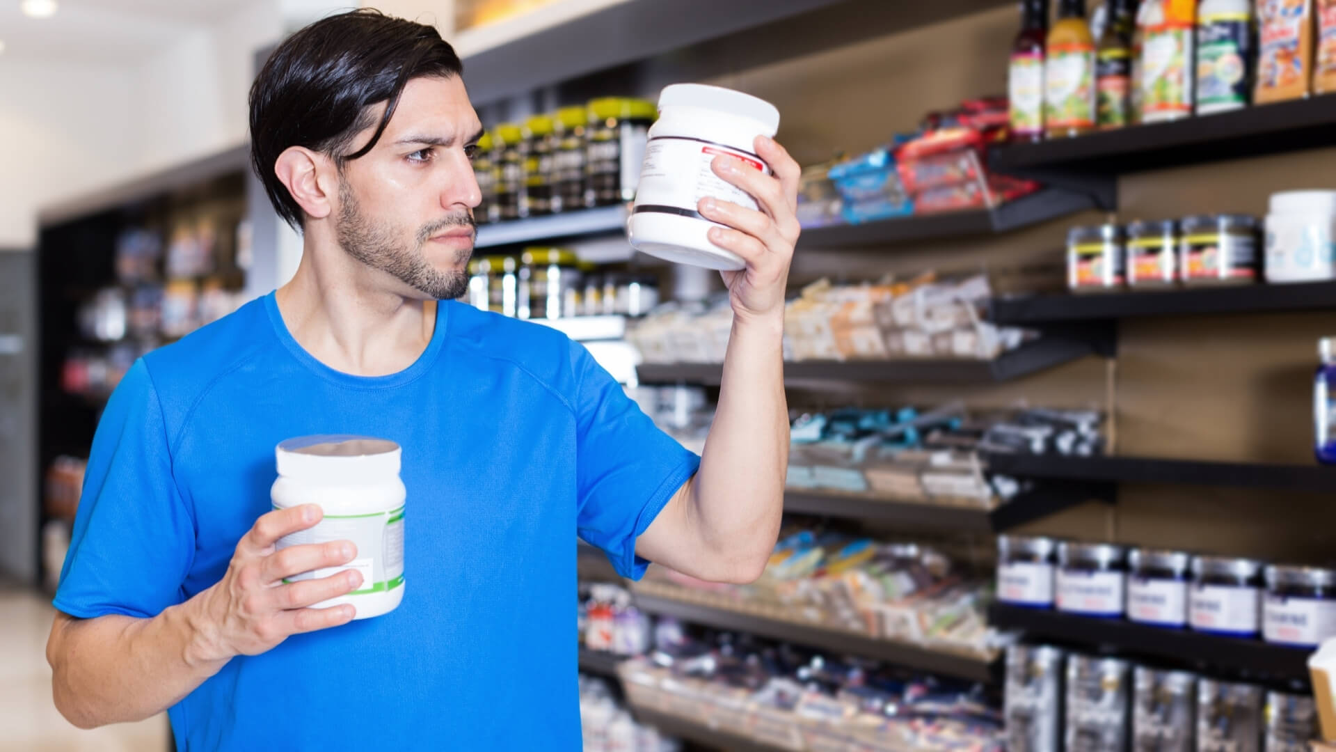 Kreatinas – Kaip Vartoti Ir Ar Jis Saugus? Kreatinas – Kaip Vartoti Ir Ar Jis Saugus?. Vyras sporto papildų parduotuvėje skaito produkto etiketę, vertindamas kreatino ar kitų papildų sudėtį prieš pasirinkimą.