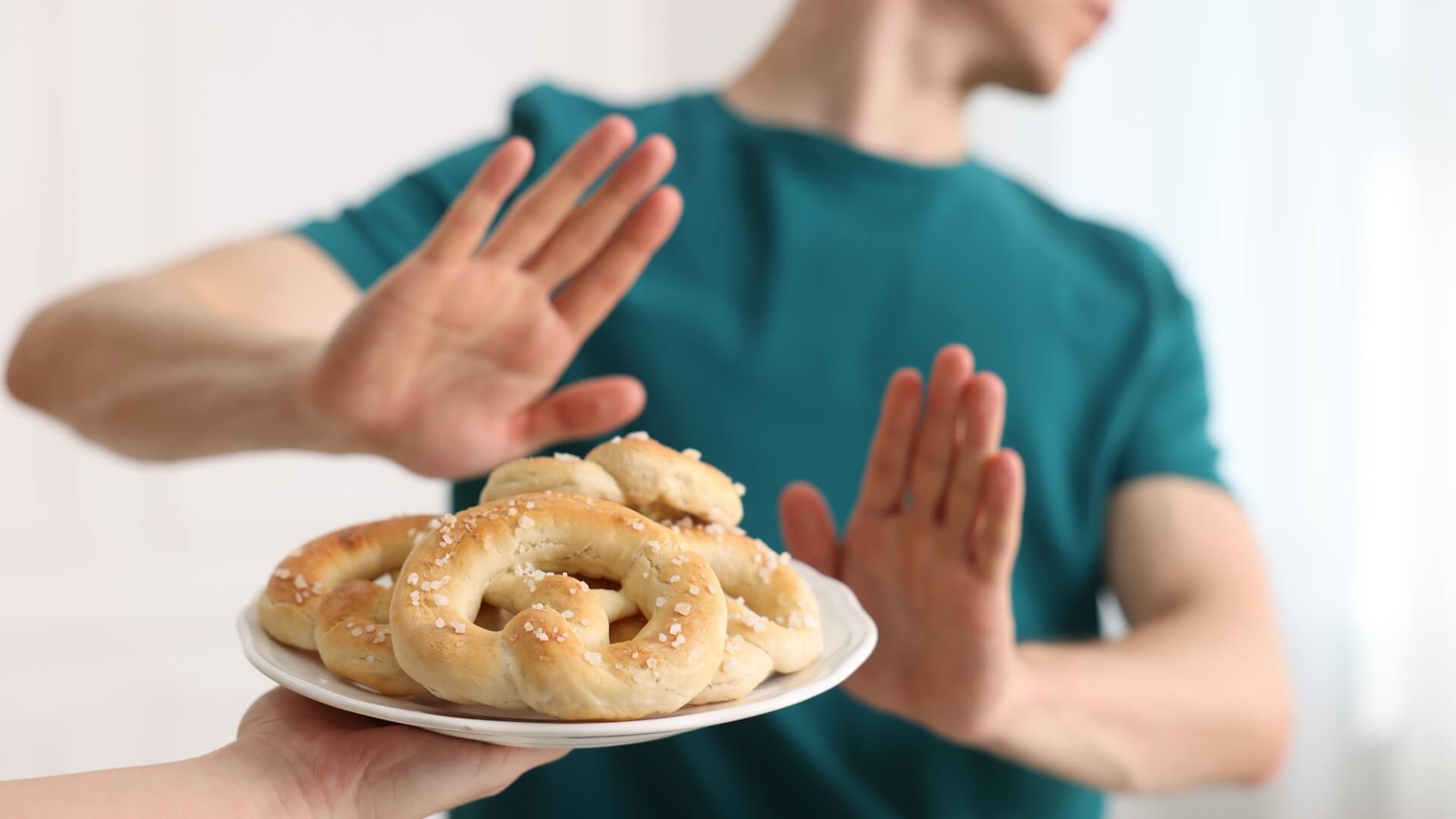 Dieta Be Gliuteno (Gluten-Free Diet) Dieta Be Gliuteno (Gluten-Free Diet). Žmogus rankomis atsisako kvietinių kepinių lėkštėje, simbolizuodamas gliuteno vengimą arba begliutenės dietos pasirinkimą.