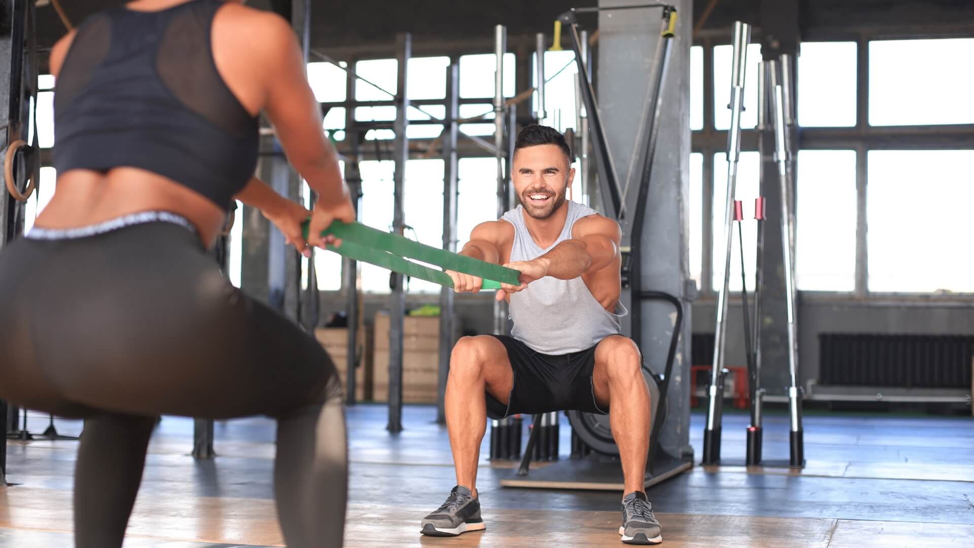 Koks Kartojimo Tempas Geriausias Raumenų Augimui? Koks Kartojimo Tempas Geriausias Raumenų Augimui?. Du žmonės sporto salėje atlieka pritūpimus naudodami pasipriešinimo gumą, lavindami kojų ir sėdmenų raumenų jėgą bei stabilumą.