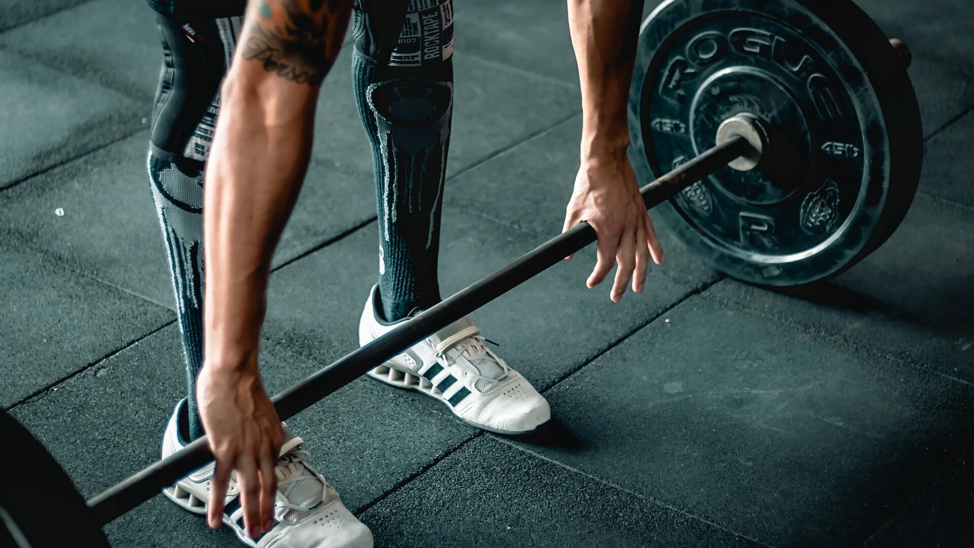Koks Kartojimo Tempas Geriausias Raumenų Augimui? Koks Kartojimo Tempas Geriausias Raumenų Augimui?. Sportininkas sporto salėje ruošiasi atlikti štangos kėlimą nuo žemės (deadlift), laikydamas štangą abiem rankomis ir lavindamas apatinės kūno dalies bei nugaros raumenų jėgą.